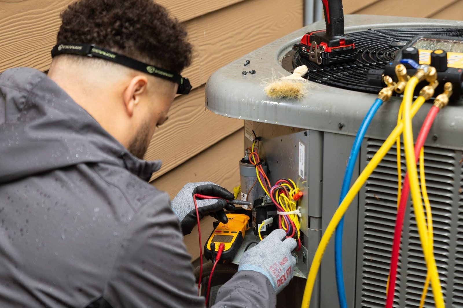 Technician testing an air conditioner with a multimeter and refrigerant gauges